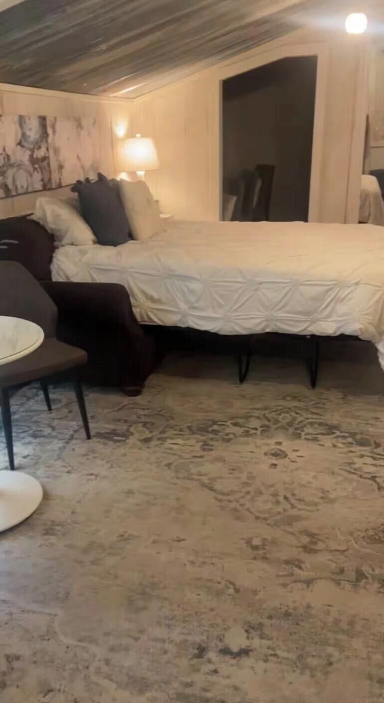 Ein Zimmer mit einem Bett, einem Sessel, einer Lampe und einem Bild an der Wand.