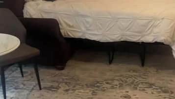 Ein Zimmer mit einem Bett, einem Sessel, einer Lampe und einem Bild an der Wand.