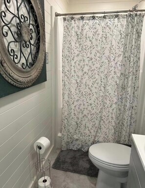 Une salle de bain comprenant des toilettes, un rideau de douche à motifs floraux, un porte-serviettes avec un rouleau de papier toilette et un élément décoratif mural.