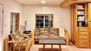 A spacious living area with a high wooden ceiling, a sofa set, a coffee table, and a bookshelf.
