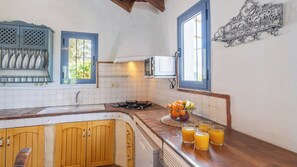 A kitchen with wooden cabinets, a gas stove, a sink, and a fruit bowl with glasses of orange juice. - Casa Rural Zambra Frigiliana by Ruralidays (Málaga)