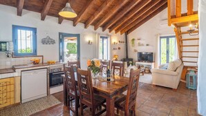 Eine rustikale Küche mit Holzbalken, einem Essbereich mit Tisch für vier Personen und einem Wohnzimmer mit Sofa und Fernseher.