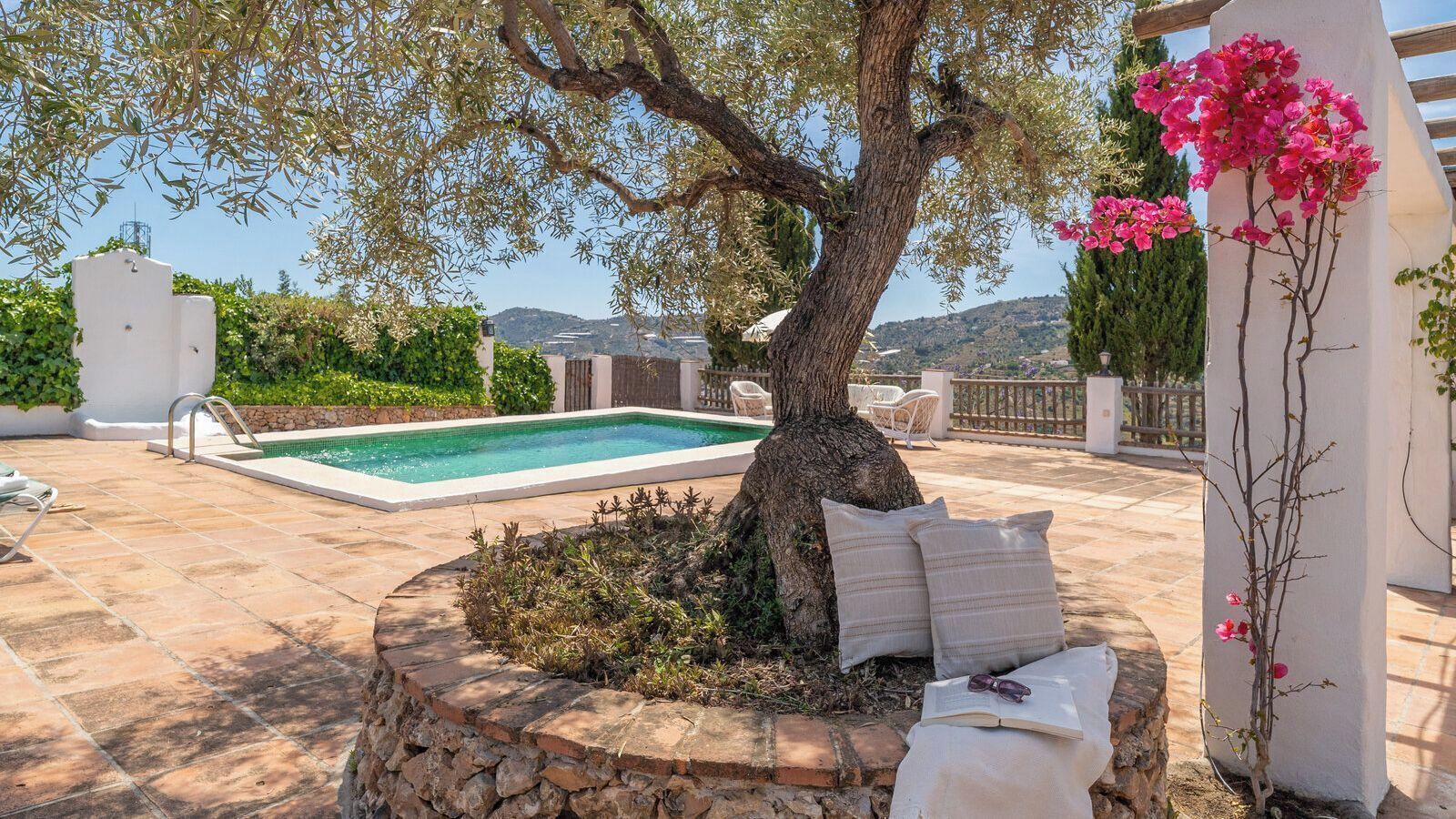 A pool area with a tree, outdoor furniture, and a view of the landscape.