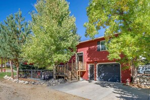 A red two-story house with a front deck, garage, and surrounding trees.