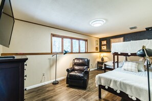 A room with a bunk bed, a leather chair, a desk with a lamp, and a window with blinds.