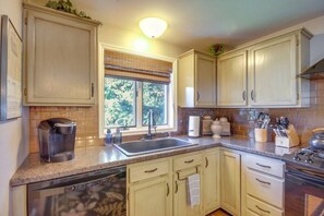 A kitchen with wooden cabinets, a built-in oven, a coffee maker, and a window with a view of trees.