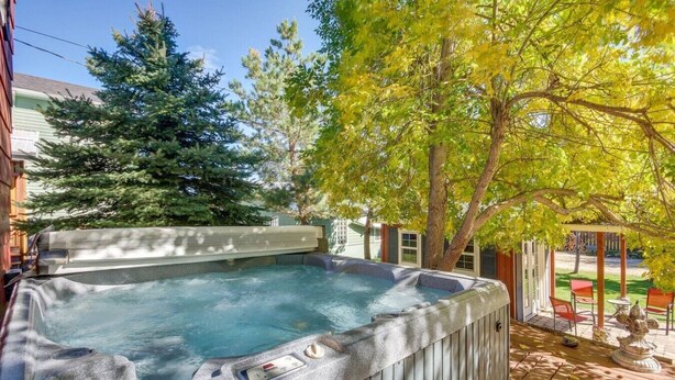 A hot tub with a control panel, surrounded by a wooden deck and a tree. - Garvey House Red | Downtown Home with Hot Tub (Red Lodge)