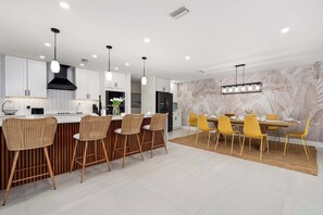 Una cocina moderna con armarios blancos, una campana extractora negra y un comedor con sillas amarillas y una mesa.