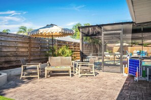 Un patio con cerramiento de madera, mobiliario exterior, una mesa y una piscina.