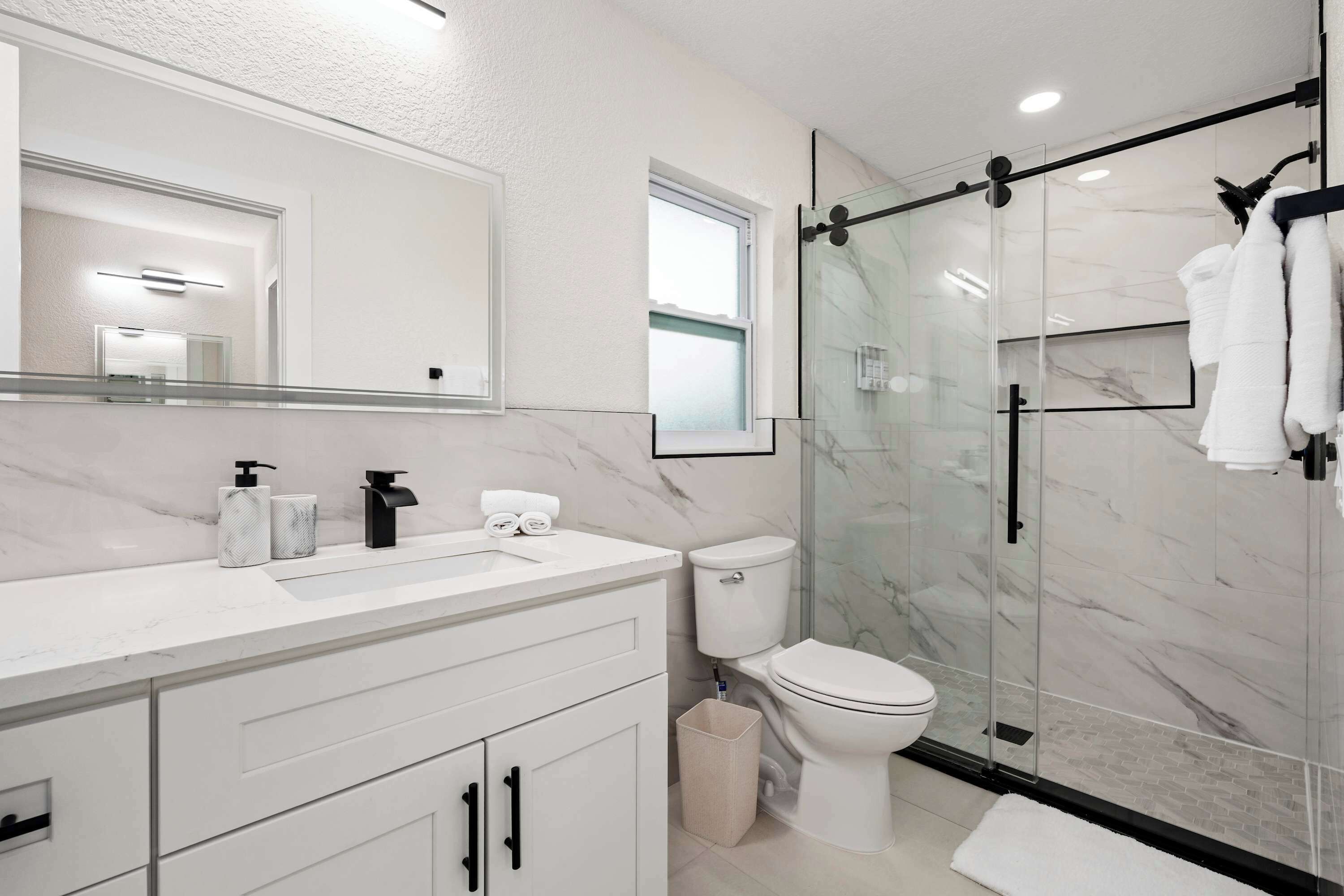 A modern bathroom with a glass shower enclosure, a white toilet, and a marble-topped sink.