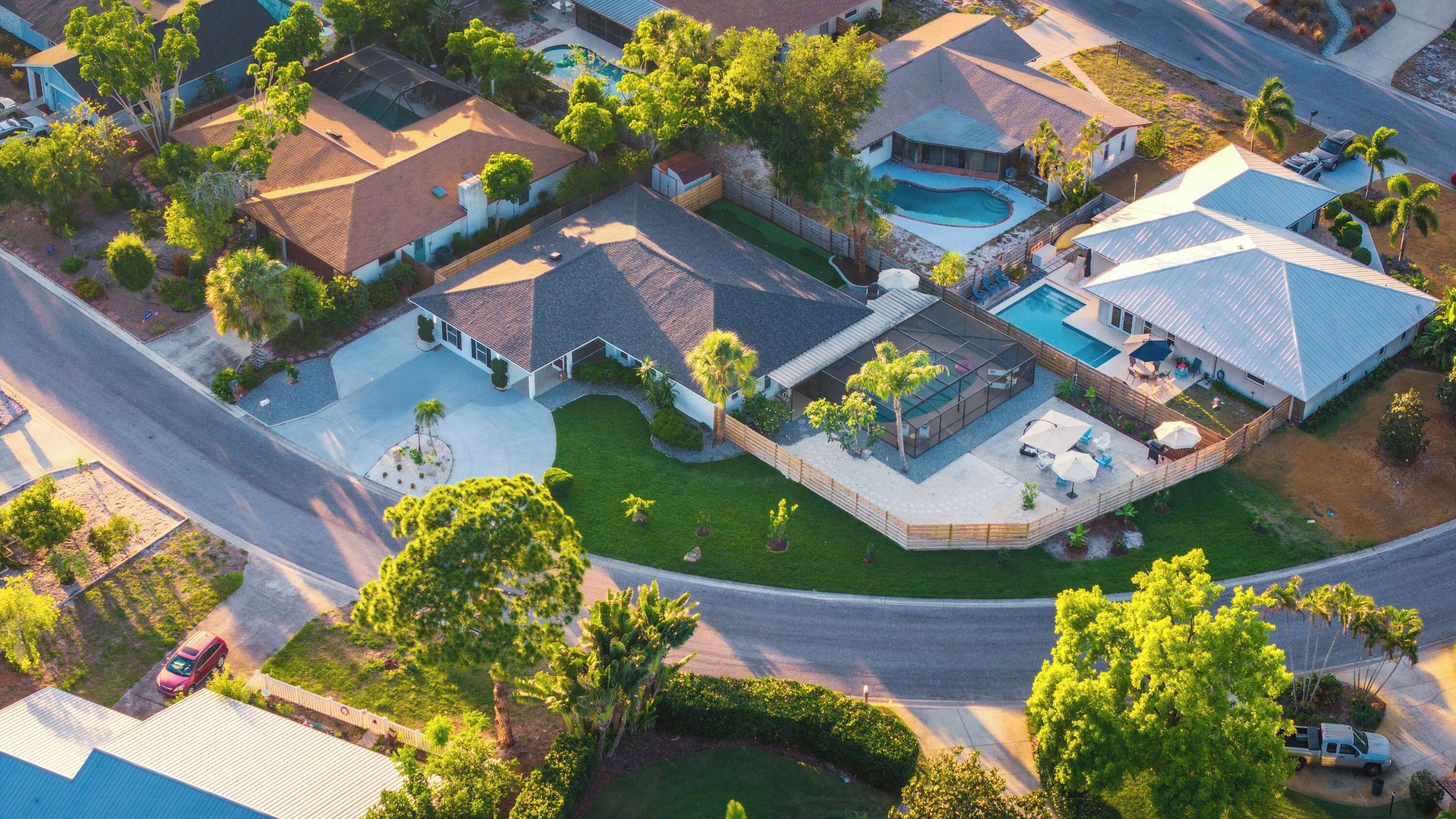 An aerial view of a residential area with multiple houses, a swimming pool, and a well-maintained lawn.