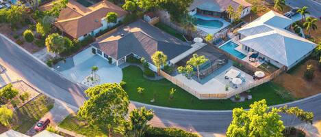 An aerial view of a residential area with multiple houses, a swimming pool, and a well-maintained lawn.