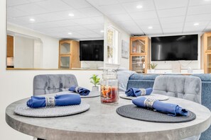 A modern living room with a round table, grey sofas, and a flat-screen TV mounted on the wall.