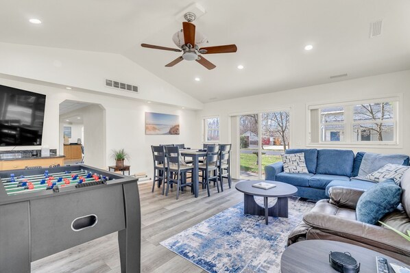 A living room with a foosball table, a blue sofa, a coffee table, and a ceiling fan.