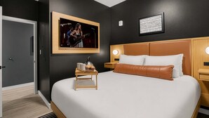 Een moderne hotelkamer met een groot bed, een nachtkastje met een lamp, een lijst met een afbeelding aan de muur, en een deur links.