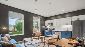 Een moderne woonkamer met een bank, salontafel en stoelen, een eettafel met een wijnglas, en een keuken met kasten en apparatuur.