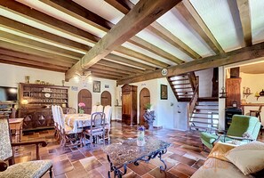 Ein geräumiger Wohnbereich mit hohen Decken, Holzbalken, einem Esstisch mit Stühlen, einem grünen Sessel und einer Treppe.