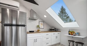 A modern kitchen with a skylight, stainless steel appliances, white cabinetry, and a wooden countertop.