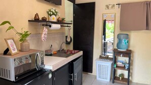 Een compacte keuken met een magnetron, spoelbak en een kleine koelkast. Er is een plank met decoratieve objecten en een waterdispenser.