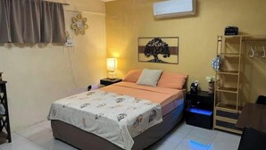 Een slaapkamer met een bed, nachtkastje, lamp, een wandairconditioner en een plank met spullen.