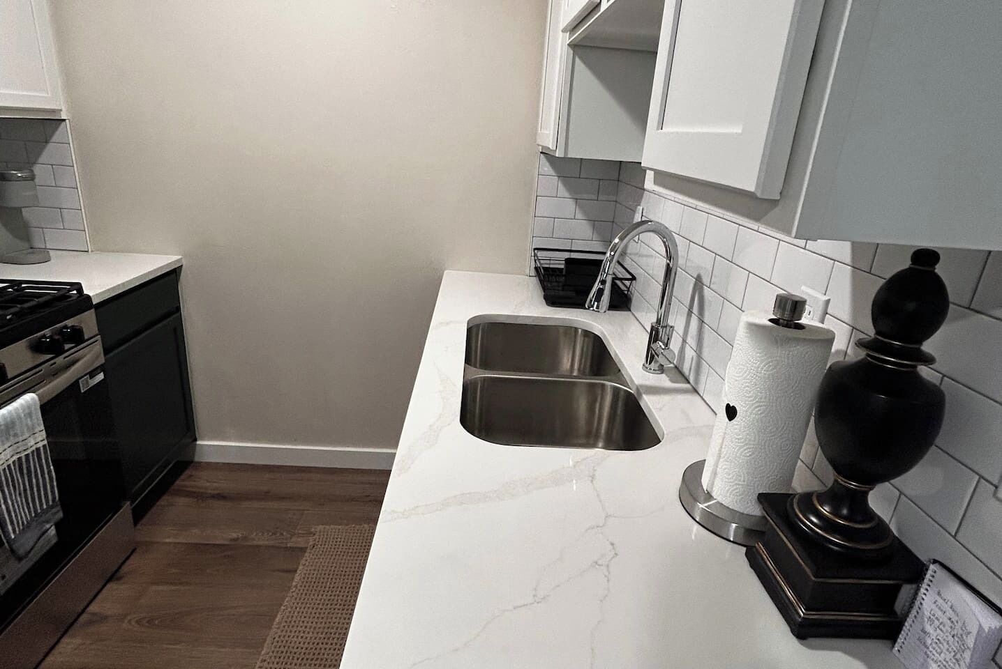 Cocina con pileta de acero inoxidable, estufa y encimeras de mármol blanco.