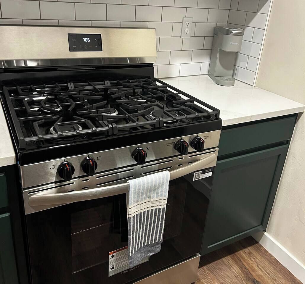 Una cocina con estufa de acero inoxidable, horno empotrado y cafetera sobre la encimera.