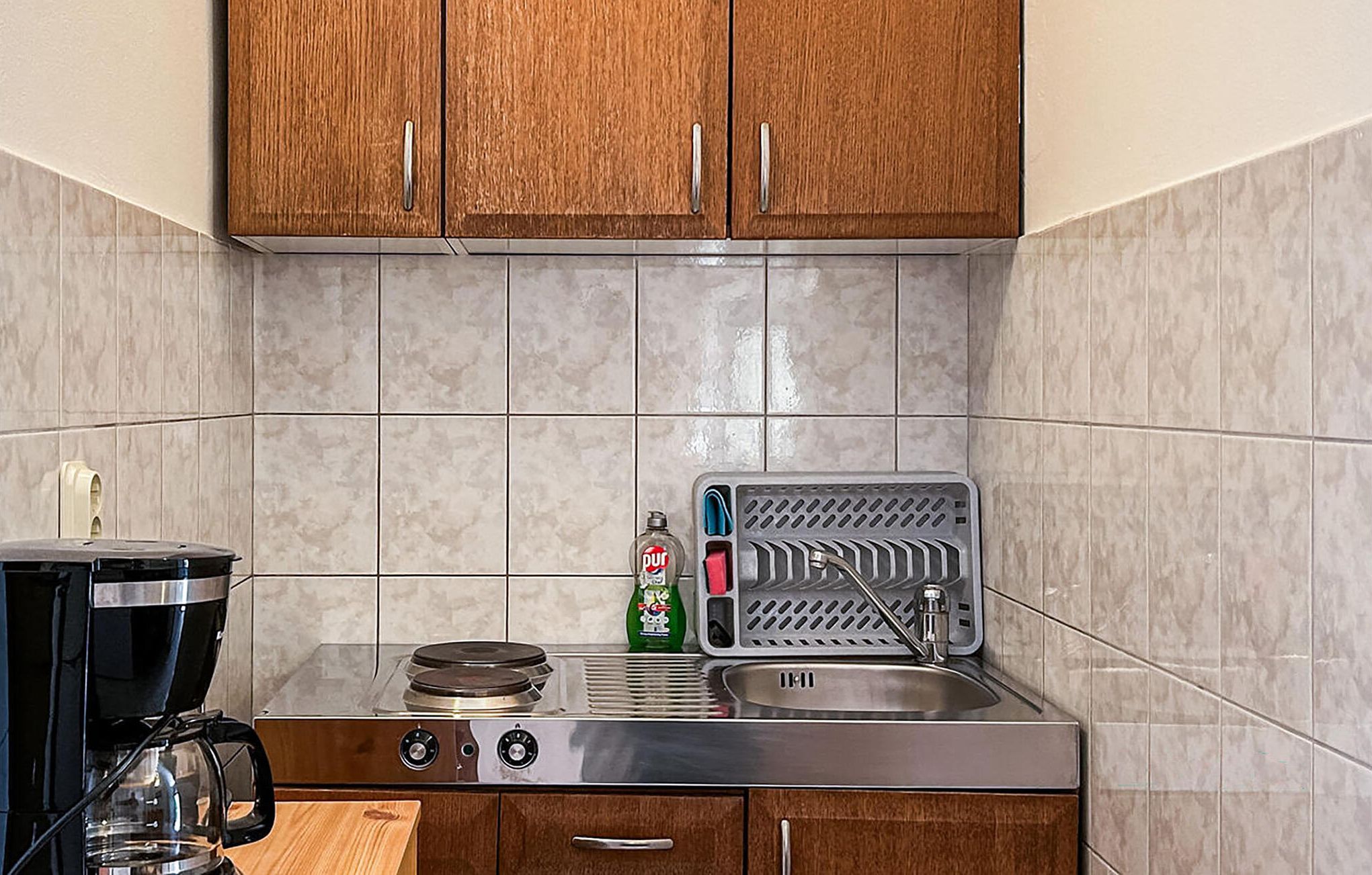 A compact kitchen with a stove, sink, and a coffee maker.