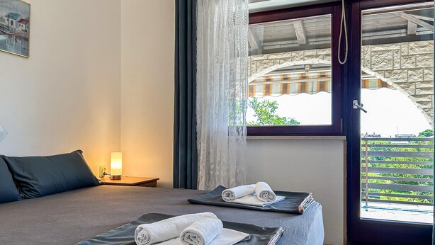 Un dormitorio con dos camas, una ventana con cortinas, una mesita de noche con lámpara y vistas al exterior.