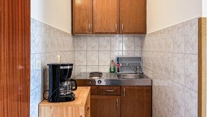 Una cocina compacta con armarios de madera, una cafetera, un hervidor y un escurreplatos.