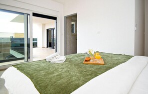 Ein Hotelzimmer mit einem Bett, einer grünen Decke, einem Tablett mit einem Croissant, Saftgläsern und einer Vase mit Blumen.