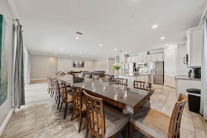 A spacious dining area with a long table and chairs, a kitchen with modern appliances, and a large window with curtains. - Fairway Royal Cottage: Near Disney, Golf Course View, Theater (Kissimmee)