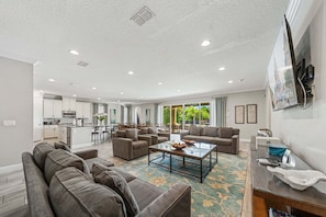 A spacious living area with a kitchen, dining area, and a large window offering a view of greenery. - Fairway Royal Cottage: Near Disney, Golf Course View, Theater (Kissimmee)