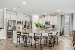 A modern kitchen with a central island, stainless steel appliances, and bar stools. - Fairway Royal Cottage: Near Disney, Golf Course View, Theater (Kissimmee)