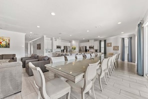 Eine moderne Küche mit weißen Schränken, ein Essbereich mit einem Glastisch und ein Wohnzimmer mit grauen Sofas.