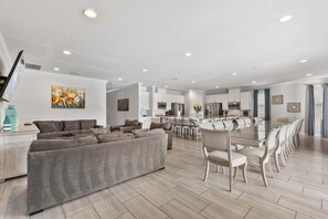 Ein modernes Wohnzimmer mit einem großen grauen Sofa, einem Essbereich mit einem Glastisch und einer Küche im Hintergrund.