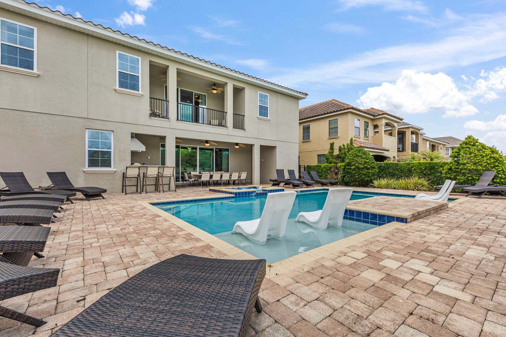 A pool area with lounge chairs, a covered seating area, and a building with balconies.