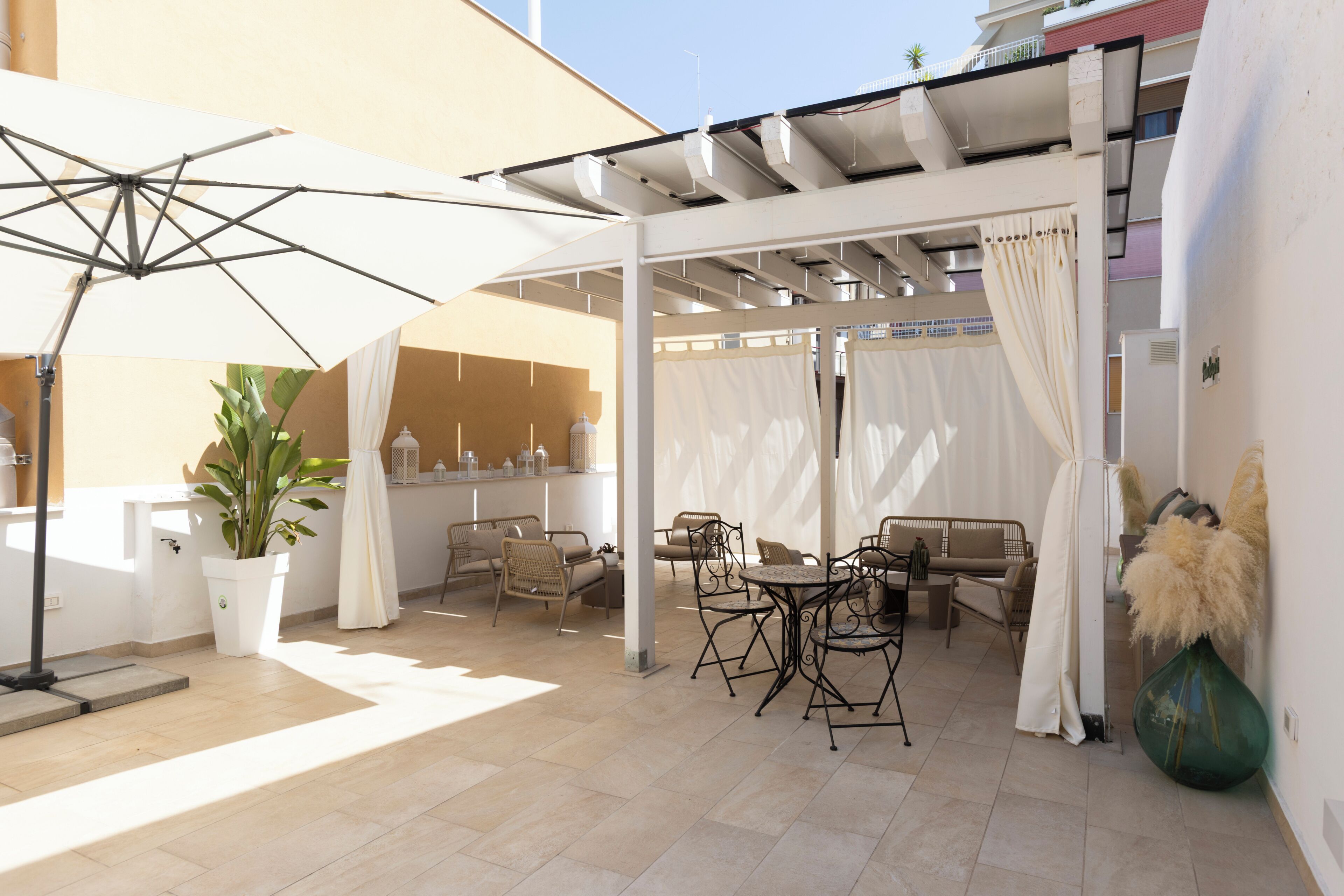 An outdoor patio with a table and chairs, a potted plant, and a large umbrella.