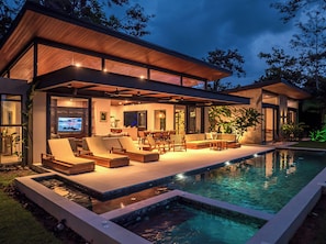 Ein modernes Haus mit Pool, Sitzgelegenheiten im Freien und einem Fernseher.