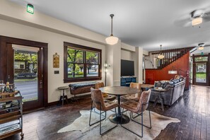 A spacious room with a round dining table, leather chairs, a bar area, and a staircase leading to an upper level. - Bluebird Day - The Annex Experience a Luxury 30 Day Stay in Bend, OR (Bend)