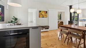 Uma cozinha moderna com máquina de lavar louça, sala de jantar com mesa e cadeiras de madeira, e vista para o exterior.