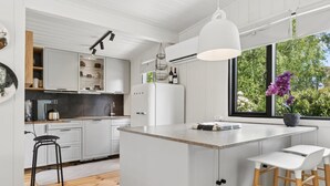 Uma cozinha moderna com armários brancos, uma ilha central, banquetas e uma janela grande com vista para áreas verdes.
