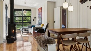 Uma sala de estar acolhedora com lareira, piso de madeira, um sofá e uma mesa de jantar com cadeiras.