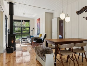 Ein gemütliches Wohnzimmer mit Kamin, Holzboden, einer Couch und einem Esstisch mit Stühlen.