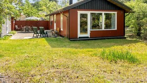 Een klein, gelijkvloers huisje met een terras en een vlonder, omringd door bomen.