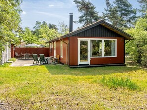 Eine kleine, eingeschossige Hütte mit Terrasse und Balkon, umgeben von Bäumen.