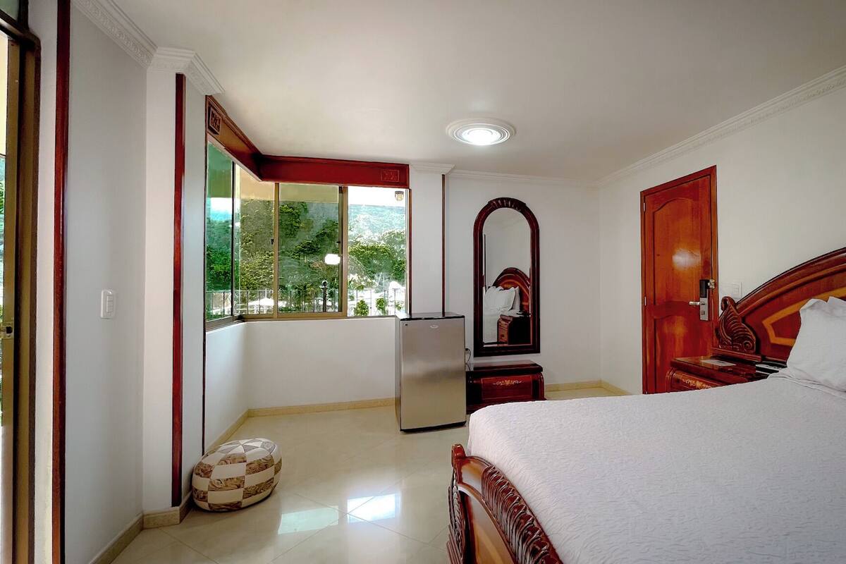 A bedroom with a bed, a mirror, a wardrobe, a small table, and a window.