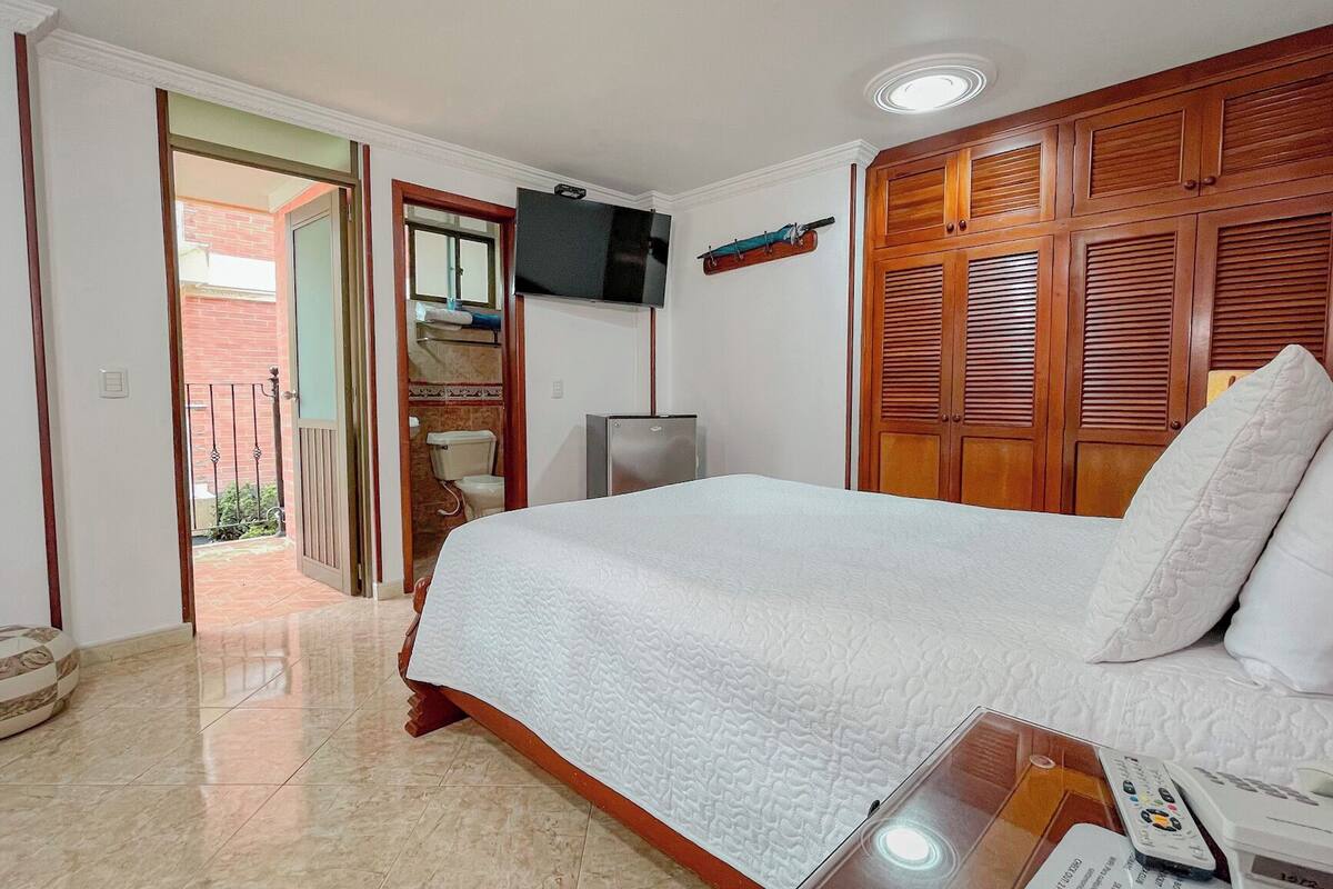 A bedroom with a bed, wooden wardrobe, television, and a small refrigerator.