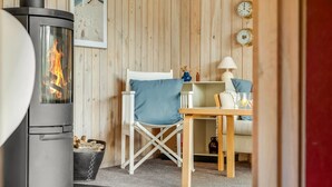 Una habitación acogedora con una estufa de leña, una silla blanca, una mesita y una lámpara.