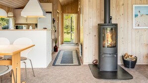 Interior acogedor de una cabaña con un estufa de leña central, una zona de cocina y un comedor.