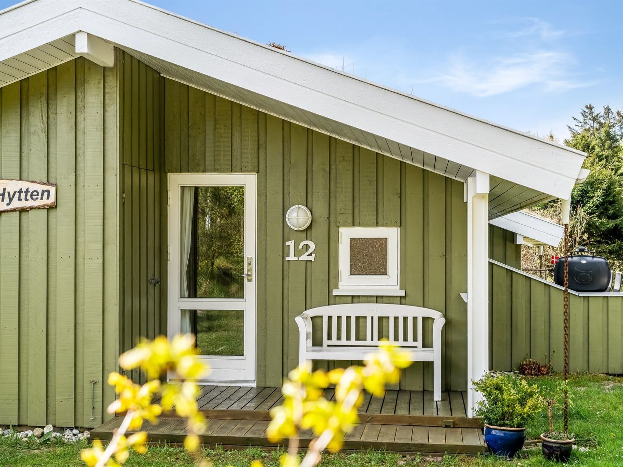 Een groen gebouw met een witte deur, een bankje en een bord met het nummer 12.